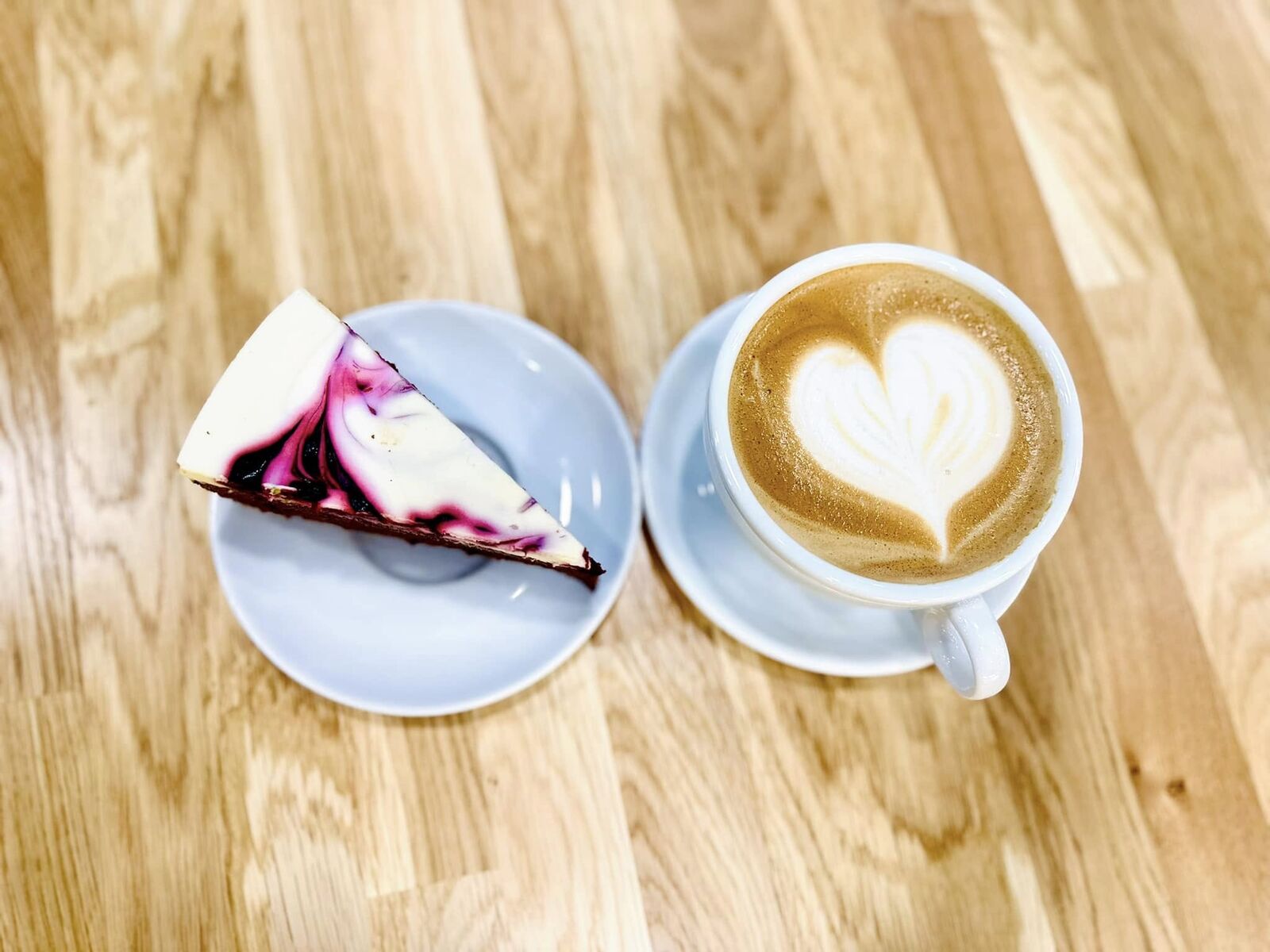 Cappuccino z latte art i kawałek sernika na drewnianym stoliku