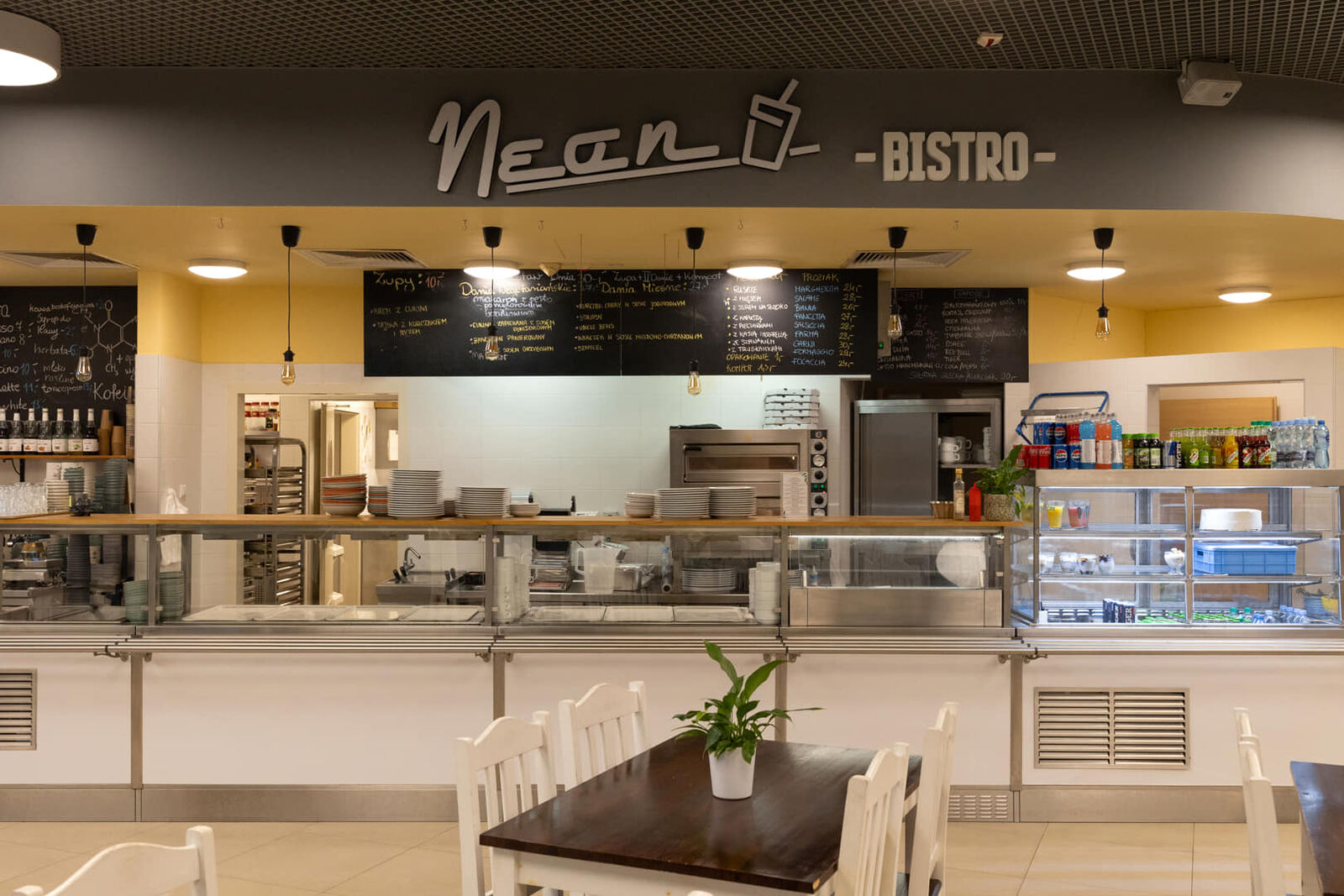 Wnętrze Neon Bistro: lada wydawcza, piec do pizzy i tablice z menu dnia