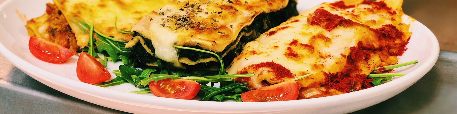 Porcje lasagne ze szpinakiem i pomidorkami na białym półmisku