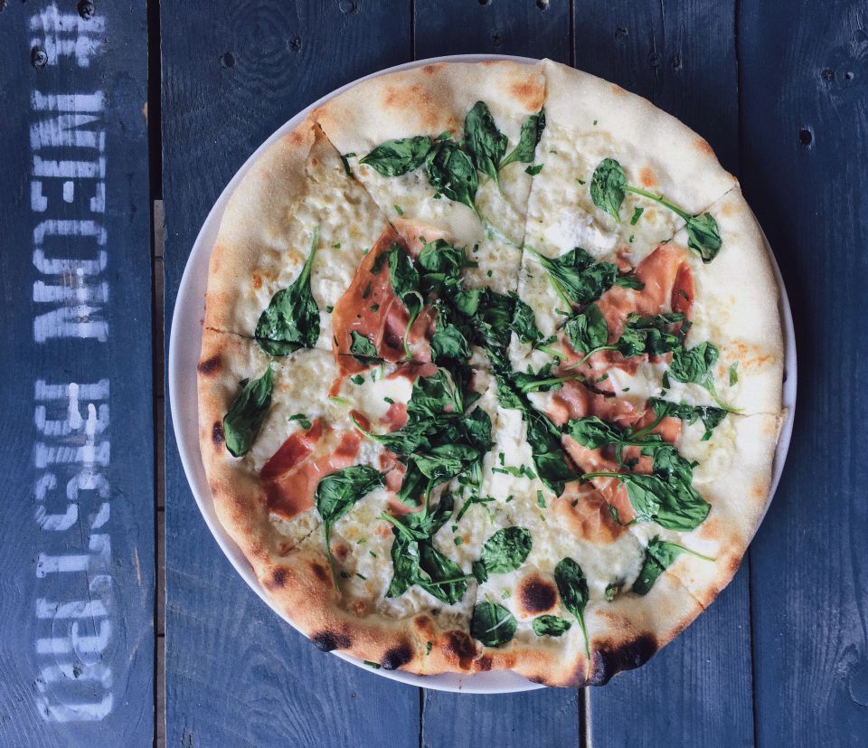 Pizza bianca ze szpinakiem i szynką na stole z napisem Neon Bistro