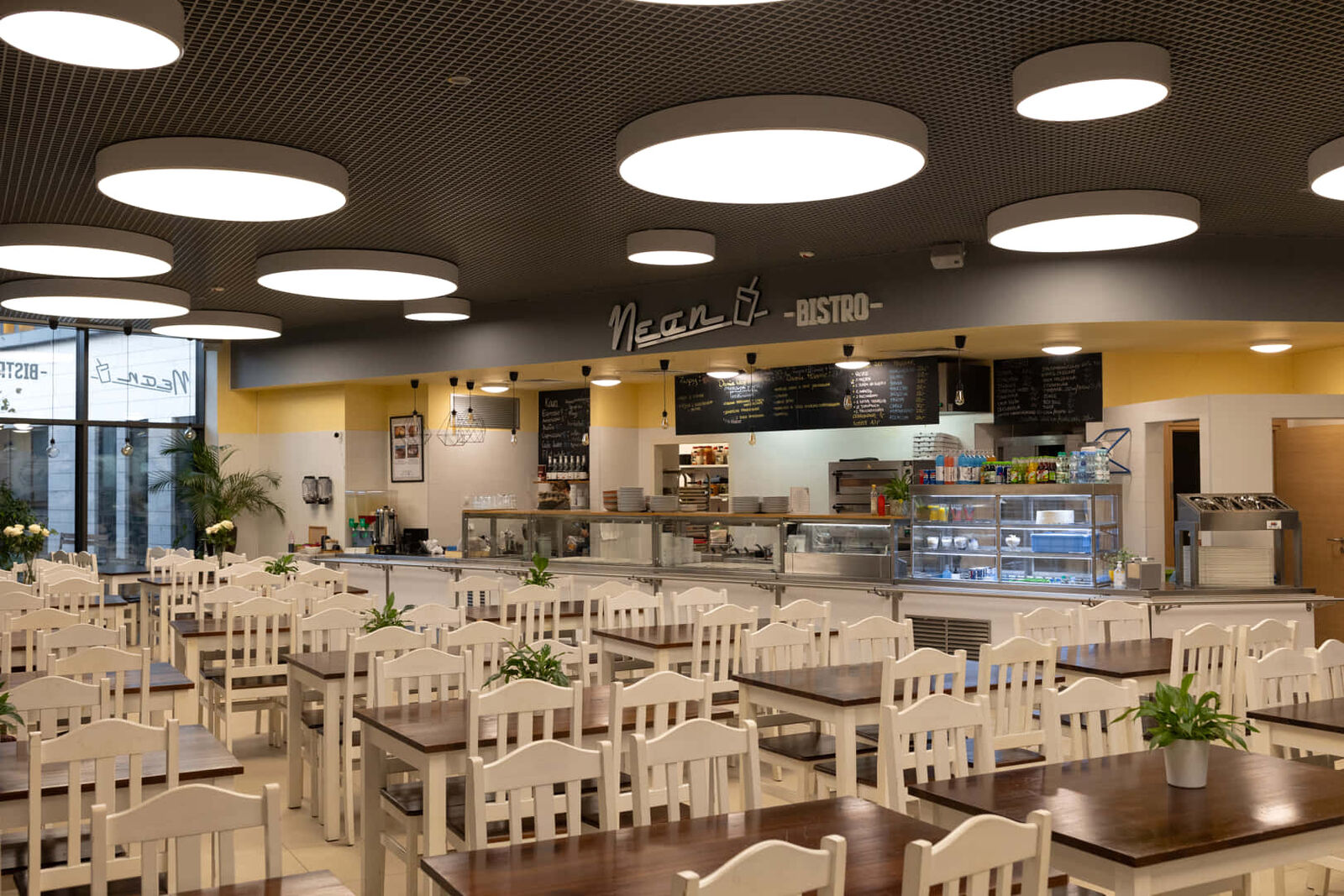 Sala Neon Bistro na kampusie UJ: białe krzesła, drewniane stoły i podświetlany napis Neon nad ladą